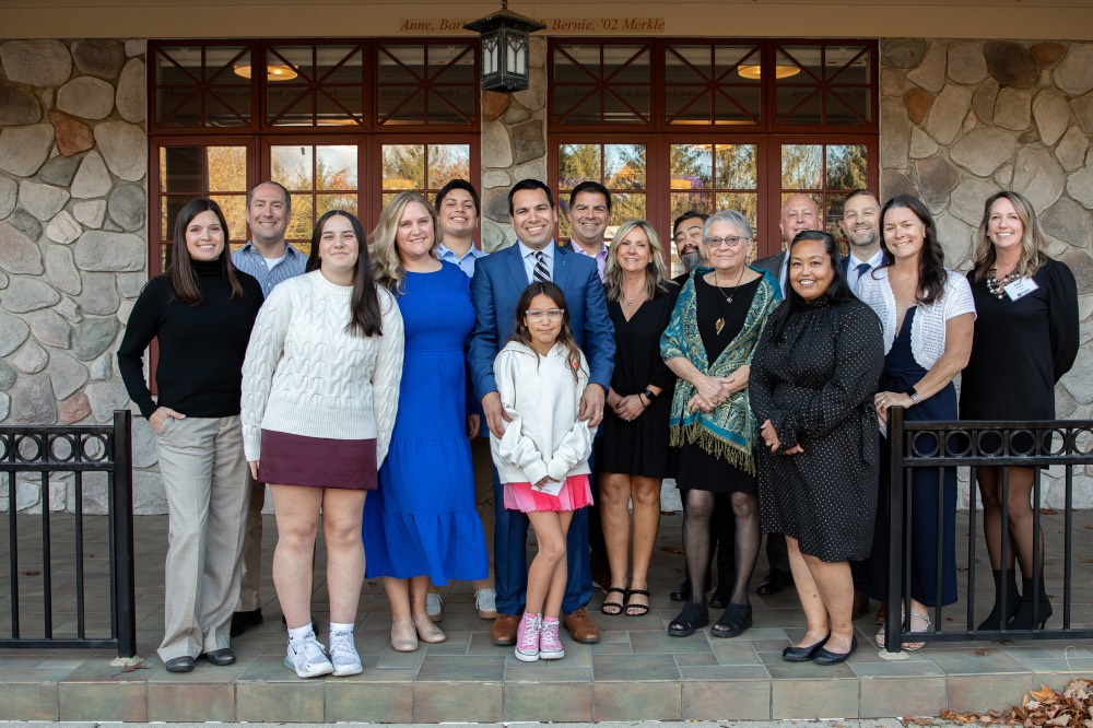Victor Cardenas poses with large group of people outside of the Alumni House